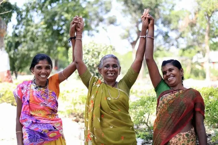 Three women standing together with raised hands in a village community
